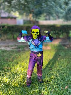 a young child dressed as a skeleton wearing purple and blue clothing, standing in the grass