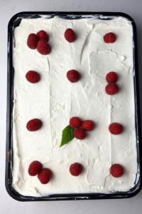 a cake with white frosting and raspberries on top is sitting in a pan