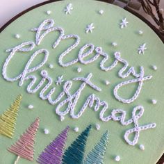 there is a cross stitch pattern on the hoop with christmas trees in different colors and letters