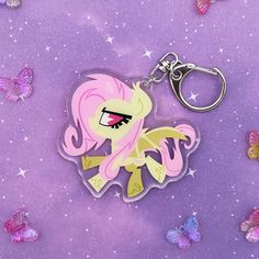 a pink pony keychain sitting on top of a purple surface with butterflies around it