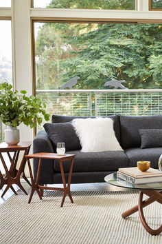 a living room filled with furniture next to a window covered in lots of plants and trees