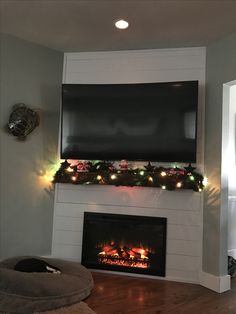 a flat screen tv mounted above a fireplace in a living room with christmas lights on the mantle