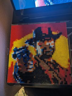 a painting made out of legos is shown in front of a television screen with the image of a cowboy on it