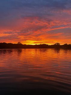 an orange and blue sunset over water with trees in the backgrounds