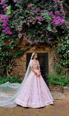 a woman in a pink and white bridal gown standing next to purple flowers on the side of a building