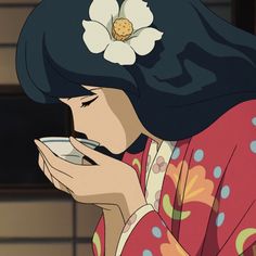 a woman with a flower in her hair drinking from a cup while wearing a kimono