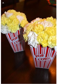 two red and white striped vases filled with yellow flowers on top of a wooden table