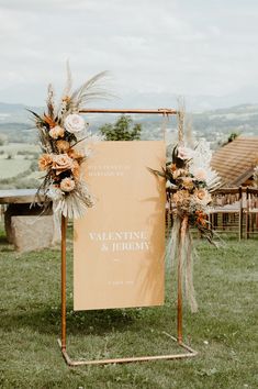 a wedding sign with flowers and greenery on it in front of a grassy field