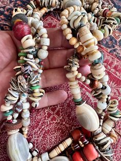 a hand is holding several bracelets made from shells and other beads on a rug