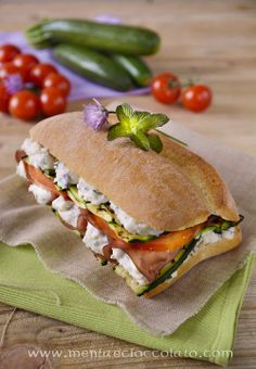 a sandwich on a napkin with tomatoes and cucumbers in the background