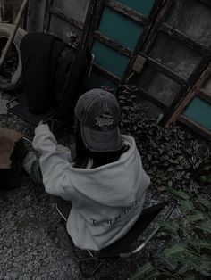 a person sitting in a chair with a hat on their head and wearing a sweatshirt