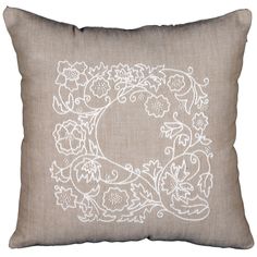 a white embroidered pillow on a brown background with an oval design in the center and flowers around it