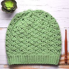 a green crocheted hat sitting on top of a wooden table next to a plant