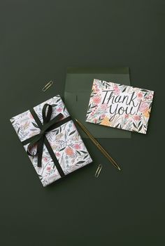 a thank you card with a gift wrapped in wrapping paper next to a note and pen