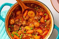 a pot filled with meat and vegetables on top of a blue towel next to a wooden spoon