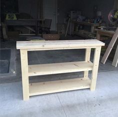 a wooden table sitting on top of a cement floor next to a pile of wood