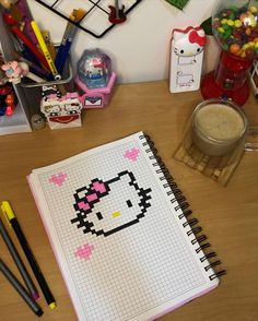 an open hello kitty notebook sitting on top of a desk next to some pens and pencils