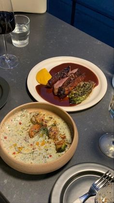 a table topped with plates and bowls filled with different types of food next to wine glasses