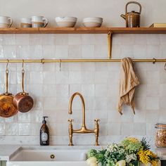 pots and pans are hanging on the wall above a kitchen sink with gold faucets