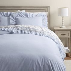 a bed with blue comforter and pillows in a white room next to a night stand