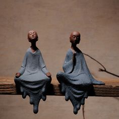 two small figurines sitting on top of a piece of wood