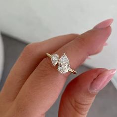 a woman's hand holding a diamond ring with two pear shaped diamonds on it