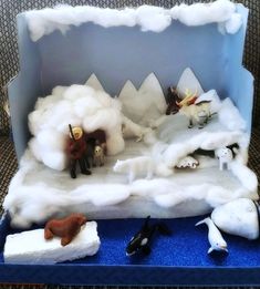 an open cardboard box with fake animals and snow on the ground in front of it