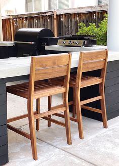 two wooden chairs sitting next to an outdoor grill