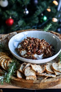 a white bowl filled with food sitting on top of a wooden platter next to crackers