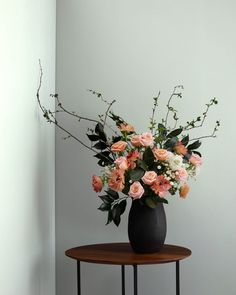 a black vase filled with pink and white flowers on top of a small round table