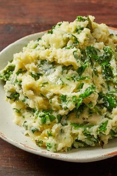 a white plate topped with mashed potatoes and spinach on top of a wooden table