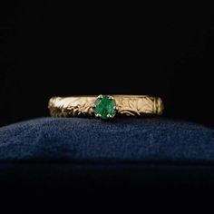 a gold ring with a green stone sitting on top of a blue velvet cushion in front of a black background