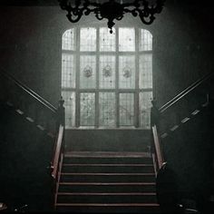 the stairs leading up to an open window in a dark room with chandelier