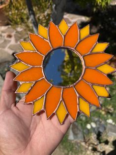 a hand holding up a sunflower shaped mirror