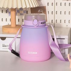 a pink and purple water bottle sitting on top of a table next to a lamp