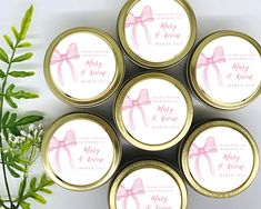 six personalized wedding candy jars with pink bows and ribbons on them, sitting next to a green plant