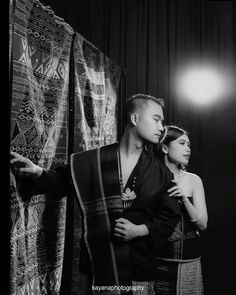 a man and woman standing next to each other in front of a wall covered with cloths