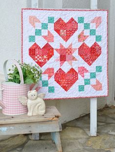 a small potted plant next to a red and green quilted wall hanging on the side of a building