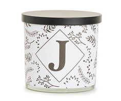 a candle with the letter j on it and leaves around it in front of a white background