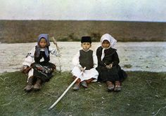 three children are sitting on the grass near water