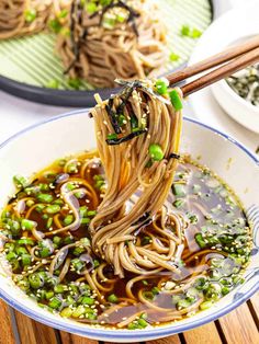 someone is holding chopsticks full of noodles with peas and sesame seeds in a bowl