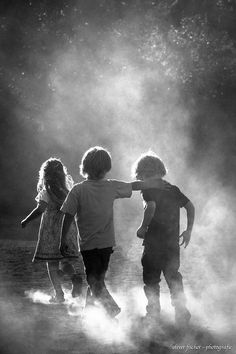 three children are playing in the dust with their arms around each other and looking at something