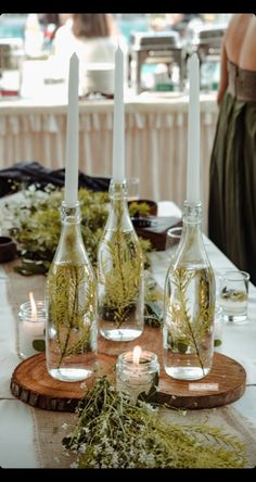 there are three bottles with plants in them on the table next to candles and flowers