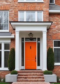 an orange door in front of a brick house with two planters on either side