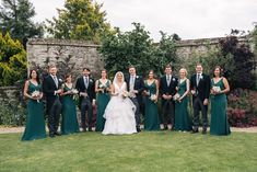 a bride and groom with their bridal party in front of an old stone wall