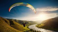 a person paragliding over a river in the mountains