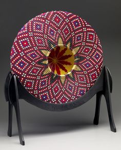 an artistically designed bowl sitting on top of a black stand with red, yellow and blue designs