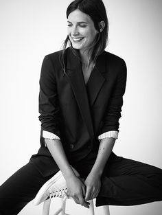 a black and white photo of a woman sitting on a stool with her legs crossed