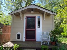 a small house with a red door and two white chairs on the front porch next to it