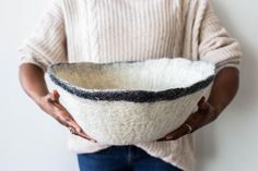 a woman is holding a bowl made out of wool